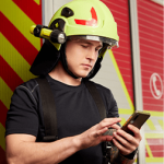 portrait-of-a-firefighter-standing-in-front-of-a-fire-engine-fireman-using-smart-phone-1